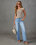 Woman wearing taupe knit keyhole top, light wash wide-leg jeans, nude heeled sandals, holding cream quilted bag with aviator sunglasses
