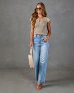 Woman wearing taupe knit cap-sleeve top, light wash wide-leg jeans, nude heels, cream woven bag, and aviator sunglasses