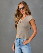 Woman wearing taupe knit crop top with keyhole detail and cap sleeves, paired with light wash jeans and aviator sunglasses
