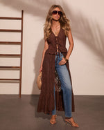 Woman wearing brown lace maxi duster over blue jeans with strappy heels, sunglasses, gold jewelry, and woven clutch bag