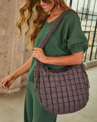 Woman wearing green loungewear set carrying large quilted charcoal puffer hobo shoulder bag with grid pattern