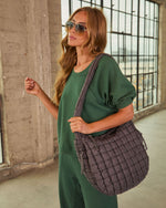 Woman in green sweatsuit wearing aviator sunglasses carrying large quilted charcoal puffer tote bag crossbody