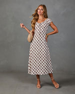 Woman wearing cream and mauve gingham midi dress with cap sleeves, tie neckline, paired with strappy heels and woven bag