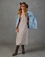 Woman wearing plaid midi slip dress with denim jacket draped over shoulders, brown cowboy hat, knee-high boots, and tinted sunglasses