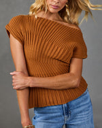 Woman wearing rust brown ribbed knit off-shoulder sweater top with blue jeans and gold earrings