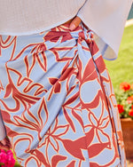 Light blue floral print wrap skirt with rust red botanical pattern, tied at waist, paired with white linen top