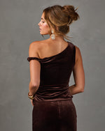 Woman in brown velvet one-shoulder top and matching pants, back view with claw clip updo, crystal earrings and gold cuff