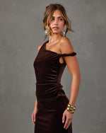 Woman in a chocolate brown velvet asymmetrical off-shoulder top and skirt with gold chunky bracelets and crystal drop earrings