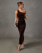Woman in a brown velvet one-shoulder maxi dress with side slit, holding a champagne coupe and clutch with clear heels