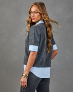 Woman modeling charcoal gray short-sleeve sweater layered over light blue collared shirt with dark jeans and gold cuff bracelet