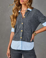 Woman wearing gray knit cardigan with gold buttons over light blue Oxford shirt, paired with dark gray jeans