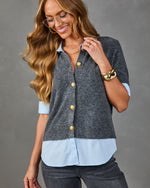 Woman wearing charcoal gray knit cardigan with gold buttons over light blue button-down shirt, styled with gold cuff bracelet and aviator glasses