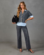 Woman wearing charcoal knit cardigan over light blue shirt, dark straight-leg jeans, black heeled sandals, holding black bucket bag