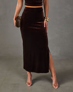 Brown velvet high-waisted maxi skirt with side slit, styled with clear heels, gold bangles and a faux fur clutch