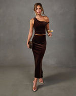 Brown velvet one-shoulder crop top and matching maxi skirt set styled with clear heels, fur clutch and a champagne coupe