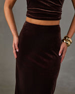 Brown velvet midi skirt and matching cropped top styled with chunky gold cuff bracelets, hands resting on hips