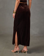 Back view of a brown velvet maxi skirt with a back slit and zipper, styled with gold cuff bracelets and nude heeled sandals