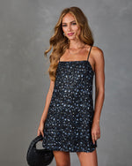 Navy blue sequin floral mini dress with spaghetti straps, worn by model holding black woven bag, party occasion wear