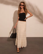 Woman wearing black ruched tube top, cream lace maxi skirt, black sandals, and woven tote bag, smiling outdoors.