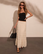 Woman wearing black ruched tube top, cream lace maxi skirt, black sandals, and woven tote bag, smiling outdoors.
