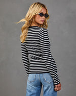 Woman wearing black and white striped ribbed long sleeve sweater with light wash distressed jeans, back view