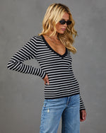 Woman wearing black and white striped long-sleeve V-neck knit top with light wash distressed jeans and black sunglasses