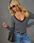 Blonde woman in black and white striped V-neck knit top, blue jeans, gold belt, black woven bag, and sunglasses