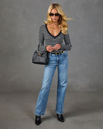 Woman wearing black and white striped long-sleeve top, light wash straight-leg jeans, black heeled boots, and woven bucket bag