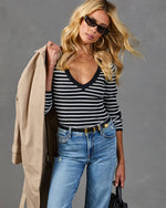 Woman in black white striped V-neck sweater, light wash jeans, beige trench coat, sunglasses, gold belt and accessories