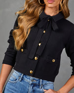 Black double-breasted knit cardigan with gold buttons and bow tie neck, styled with light wash denim jeans