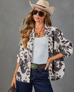 Woman wearing cow print shacket over white tank, dark jeans, turquoise belt buckle, cowboy hat, and aviator sunglasses
