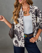 Woman wearing open cow print shacket over white bodysuit with dark jeans, turquoise concho belt, and woven leather bag