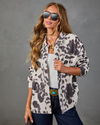 Woman wearing cream and gray cow print shacket, white tank, dark jeans, turquoise belt buckle, gold hoops, aviator sunglasses
