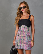 Woman wearing black bustier mini dress with multicolor tweed skirt, cat-eye sunglasses, gold jewelry, holding black woven bag