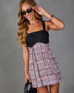 Woman wearing black and pink multicolor tweed mini dress with square neckline, sunglasses, gold cuff bracelet, holding woven clutch