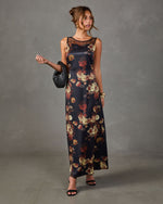 Sleeveless black satin maxi dress with red and gold floral print, sheer mesh neckline, styled with black sandals and woven clutch