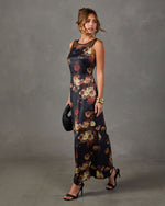 Black satin maxi dress with red and cream floral print, sheer mesh neckline, styled with gold cuff bracelets and black heels