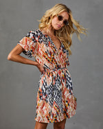 Woman wearing colorful ikat print mini dress with elastic waist, short sleeves, V-neckline, styled with gold hoop earrings and sunglasses