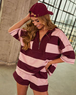 Woman wearing burgundy and pink striped quarter-zip pullover top and matching shorts set with coordinating burgundy baseball cap