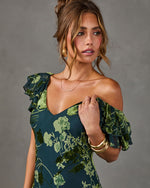 Woman in a dark green floral velvet burnout dress with ruffle off-shoulder sleeves, gold bangles, and a delicate gold necklace