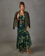 Woman in a green floral velvet burnout maxi dress with olive suede jacket, brown studded belt, gold cuffs and tan western boots