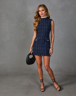 Woman wearing navy tweed mini dress with gold buttons, lace collar, black strappy heels, and woven leather hobo bag