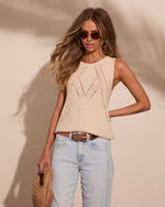 Woman wearing cream pointelle knit tank top with light wash jeans, brown belt, woven bag, and gold hoop earrings