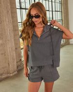 Woman wearing charcoal gray quarter-zip crop sweatshirt and matching drawstring shorts set with dark sunglasses