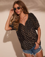 Woman wearing black boho floral print V-neck top with distressed denim shorts, gold jewelry, and oval sunglasses