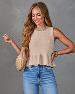Woman wearing beige knit peplum sweater tank with rhinestone neckline, blue jeans, woven bag, and gold cuff bracelet