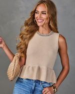 Woman wearing beige knit peplum sweater tank with jeweled neckline, blue jeans, woven bag, and gold accessories