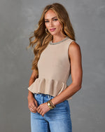 Woman wearing beige knit peplum sleeveless top with jeweled neckline and blue jeans, styled with gold bracelets and hoop earrings