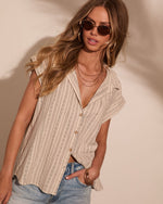 Woman wearing beige striped linen button-down top with gold jewelry, sunglasses, and light wash denim jeans