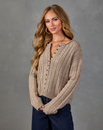 Woman wearing ribbed knit henley sweater in taupe with button detail, paired with dark wide-leg jeans